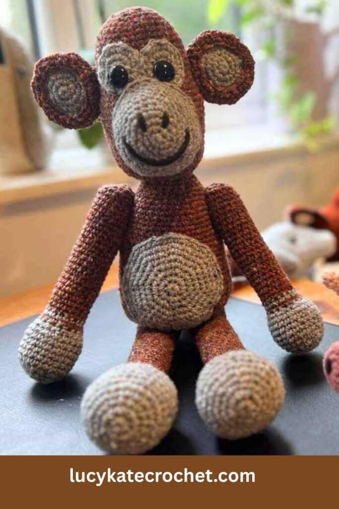 photo of a crochet monkey sitting on a desk in front of a window
