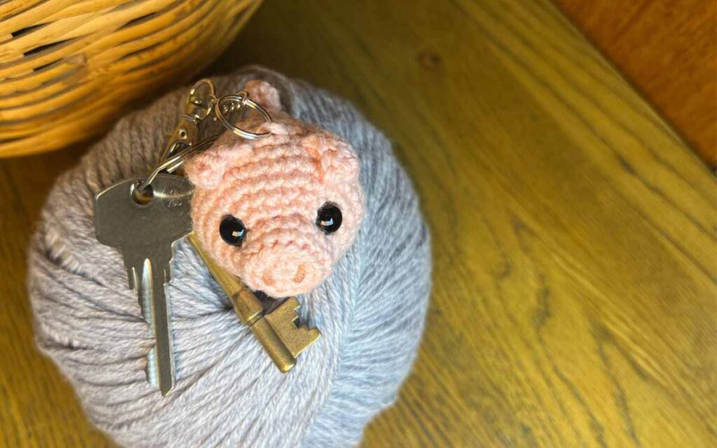 image of the amigurumi pig keychain on some gray yarn