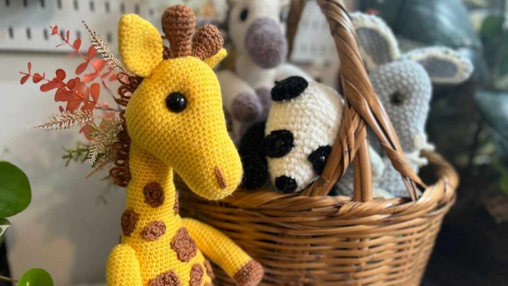 closeup photo of the crochet giraffe next to a basket of amigurumi
