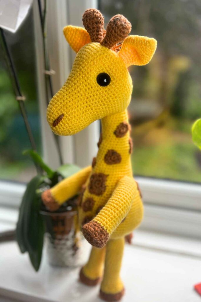 photo of the amigurumi giraffe standing on a window sill