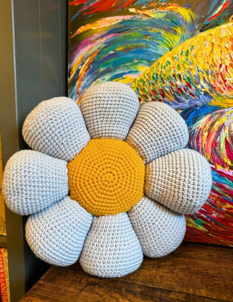 The crochet flower pillow next to a painting