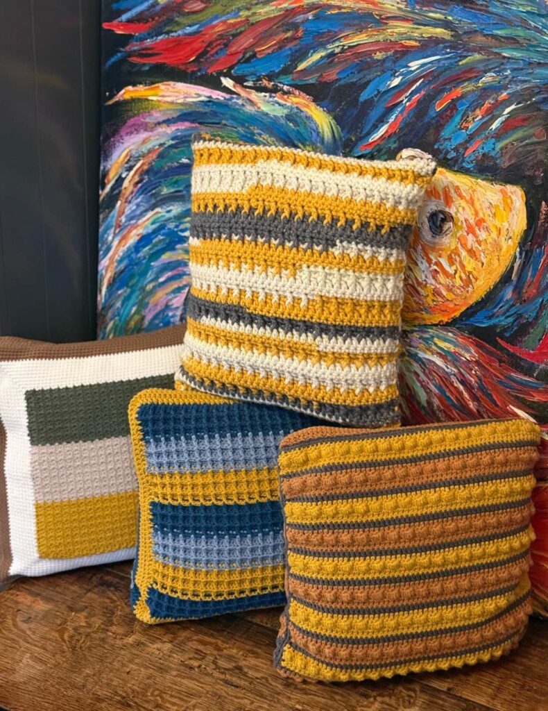 four crochet pillows beside a painting