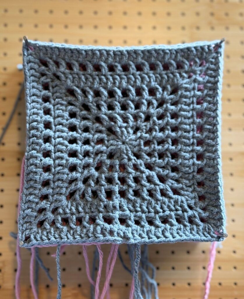 grey granny square on a blocking board